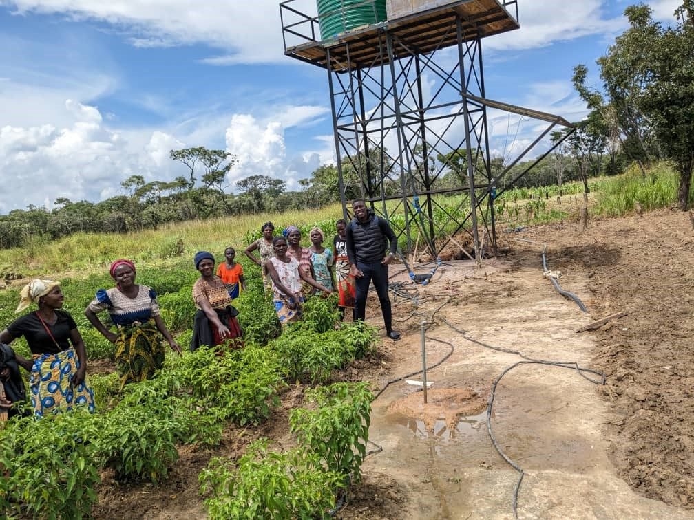 Community members at an irrigated vegetable garden beside a raised water tank tower